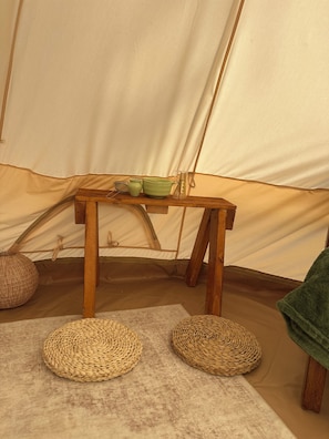 Interior d'una tenda amb taula de fusta, esteves teixides i drap verd.
