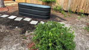 Un espace jardin aménagé avec un bac noir, des pas japonais et une clôture en bois.
