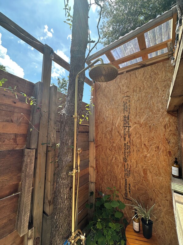 A wooden outdoor shower area with a tree, wooden walls, and a metal showerhead.