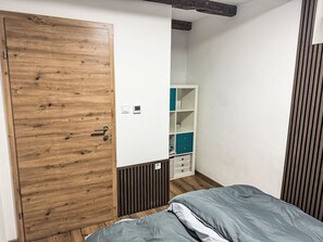 Ein Schlafzimmer mit einem Holzschrank, einem Bett mit grauer Bettwäsche und einer weißen Wand mit Thermostat.