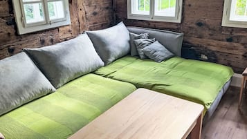 A wooden interior with a green sofa, a wooden table, and two windows.