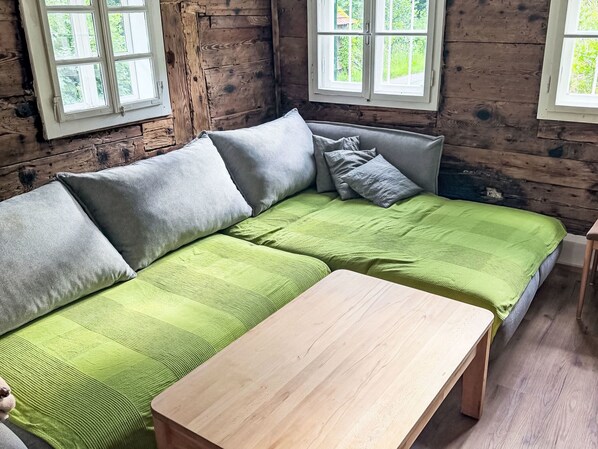 Un interior de madera con un sofá verde, una mesa de madera y dos ventanas.