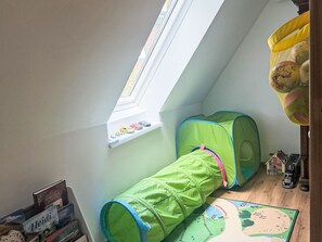 Ein Spielbereich für Kinder mit einem Fenster, einem grünen Tunnel und einem kleinen Haus.