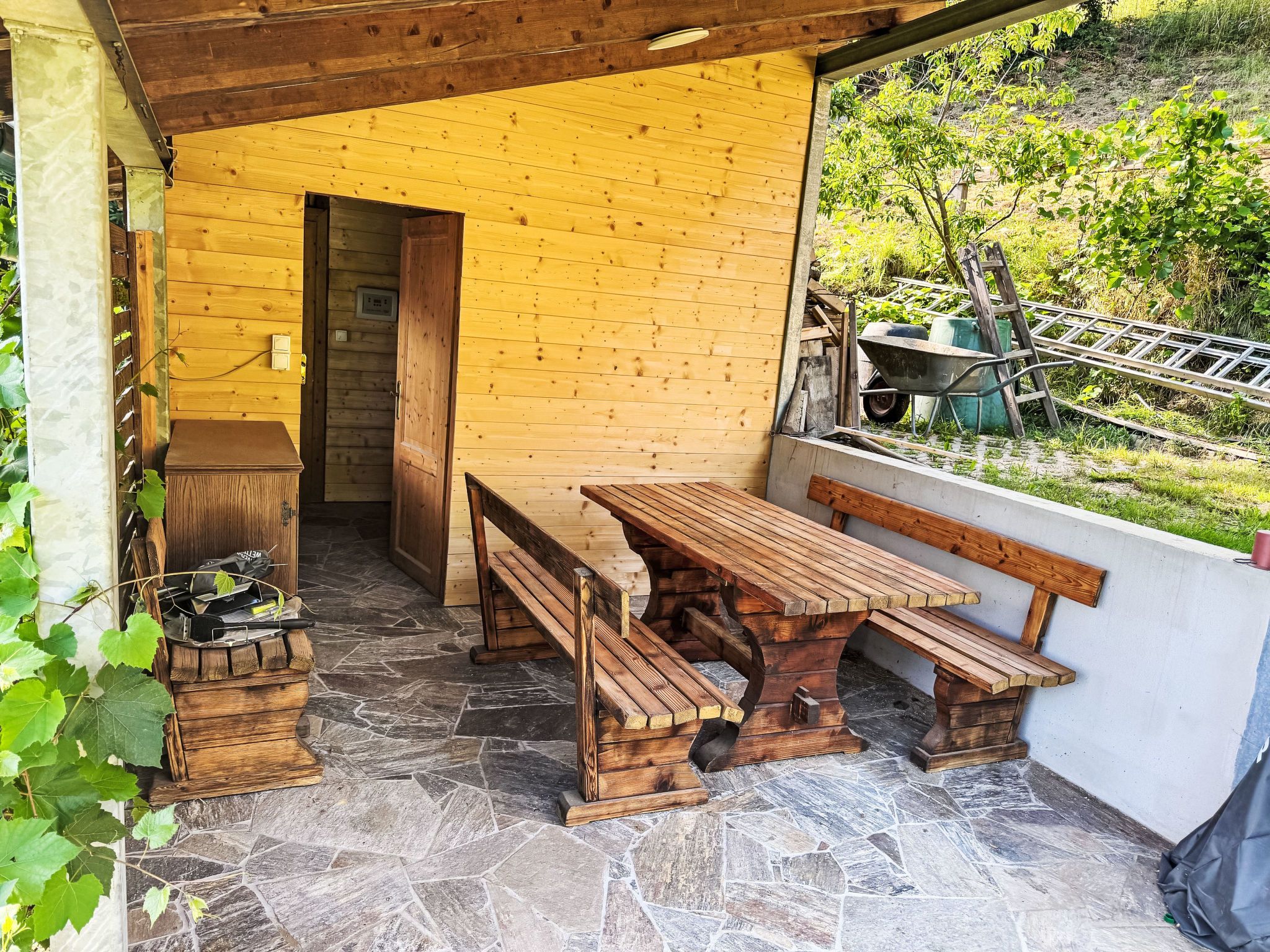 Ein hölzerner Sitzbereich im Freien mit Steinboden, einer Holzbank und einem Tisch.