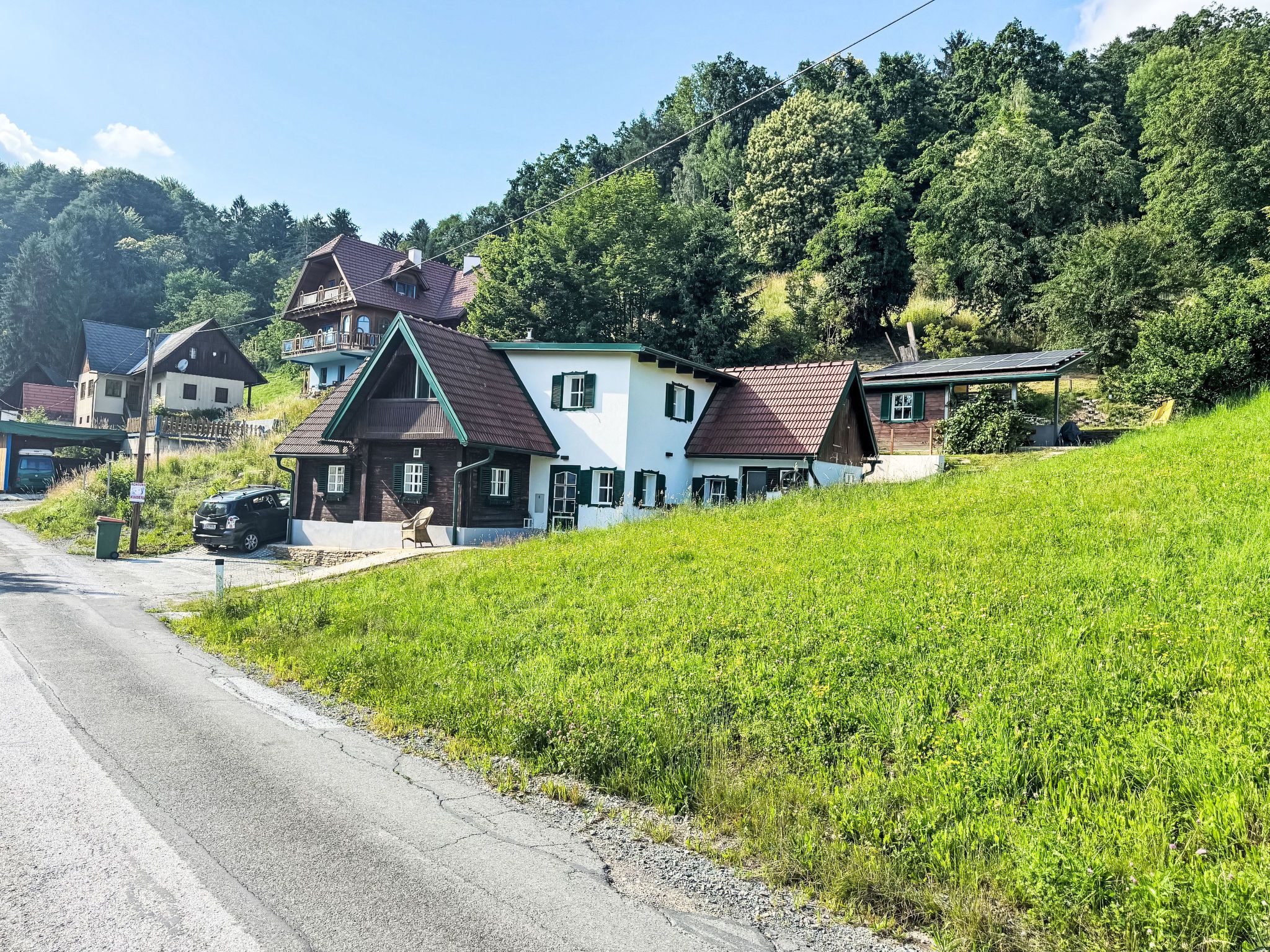 A rural road with houses on a hillside, a gravel shoulder, and a green field.