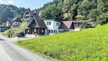 A rural road with houses on a hillside, a gravel shoulder, and a green field.