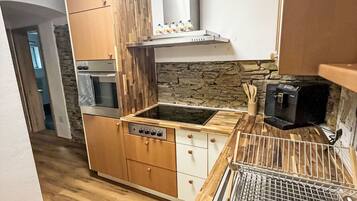 A compact kitchen with wooden cabinets, a built-in oven, a microwave, and a stone backsplash.