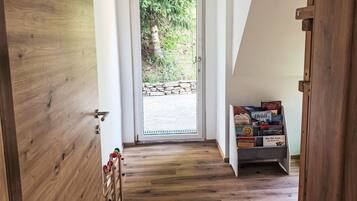 A wooden interior hallway leading to a glass door with a stone wall outside. A small shelf with books is visible.