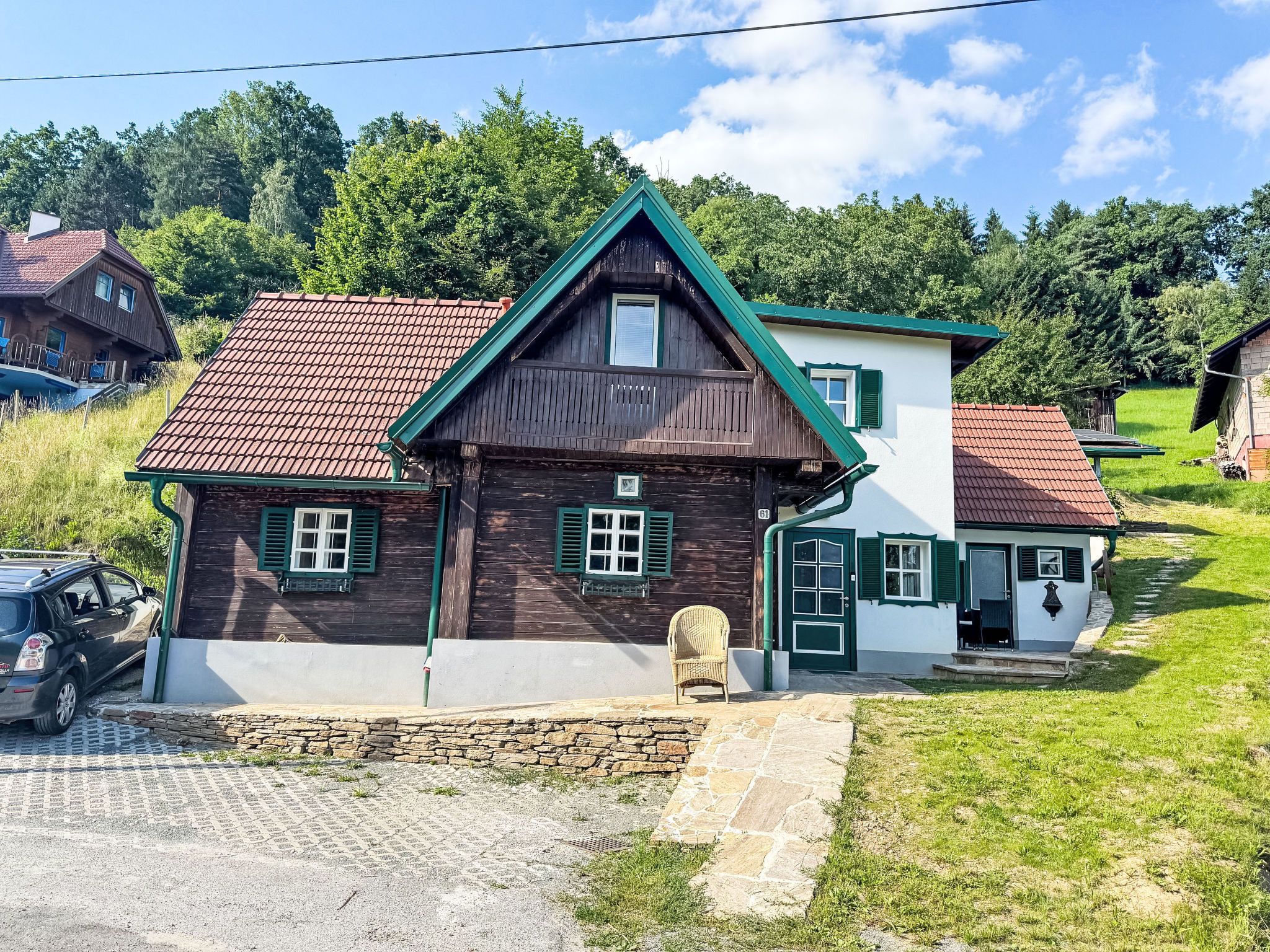 Ein zweistöckiges Haus mit einem steilen Walmdach, einem Steinfundament und einer kleinen Veranda.