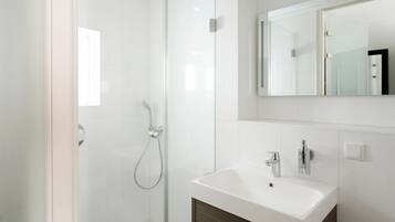 Een moderne badkamer met een douchecabine van glas, een wit wastafelmeubel en een spiegel erboven.