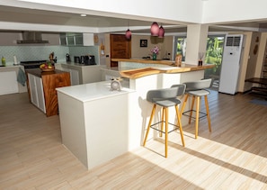 A modern kitchen with a central island, bar stools, and a view of the living area. - Tropical 4BD Villa, just 50 m from the beach. (Koh phangan)