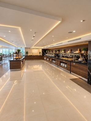 Un área de buffet moderna y bien iluminada, con mostrador de mármol, diversas opciones de comida y una zona de estar con mesas y sillas.