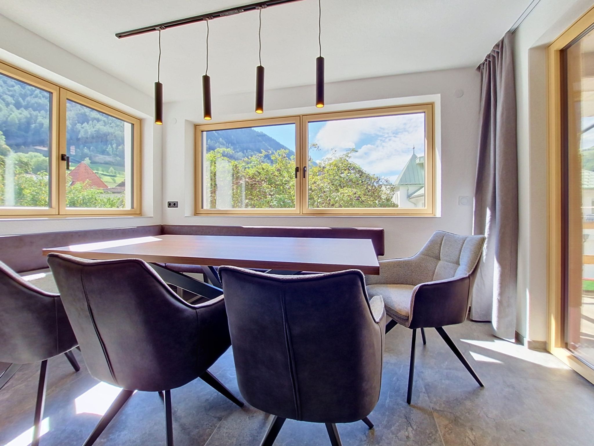 Un espace de restauration moderne avec une longue table, des chaises noires et de grandes fenêtres offrant une vue sur les montagnes.