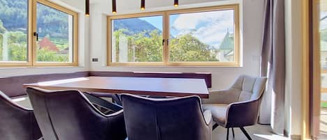 Un espace de restauration moderne avec une longue table, des chaises noires et de grandes fenêtres offrant une vue sur les montagnes.
