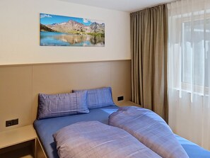 Et hotelværelse med en seng, et billede af en bjerg sø og et vindue med gardiner.
