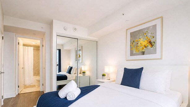 A hotel room with a bed, a mirror, a nightstand, a lamp, and a painting on the wall. - StayToronto - Modern Bay Apartments (Toronto)