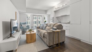 A modern living room with a sofa, coffee table, and TV. There is a kitchen area with cabinets and a countertop. - StayToronto - Modern Bay Apartments (Toronto)