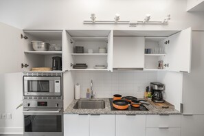 Una cucina moderna con mobili bianchi, forno ventilato, microonde e macchina per il caffè.