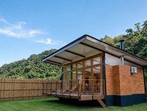 A modern building with a glass facade, wooden deck, and a view of a forested hill. - Recanto conexões  (Santo Antônio do Pinhal)