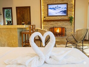 A hotel room with a fireplace, a television mounted above it, and a bed with two swan-shaped towels. - Recanto conexões  (Santo Antônio do Pinhal)