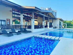 Piscina com espreguiçadeiras e área coberta com vista para um edifício.