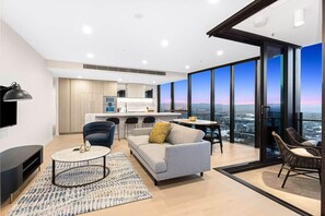 Ein modernes Wohnzimmer mit einer Couch, einem Couchtisch und Sesseln, einer Küchenzeile und großen Fenstern mit Blick auf die Stadt.