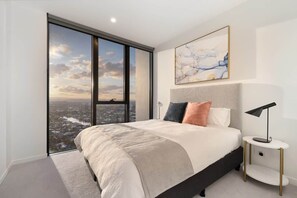 Un dormitorio moderno con un ventanal grande, una cama con cabecera y una mesita de noche con una lámpara.