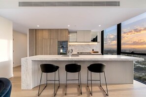 Una cocina moderna con encimera de mármol, tres taburetes negros y un ventanal con vistas a la ciudad.