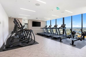 Ein Fitnessstudio mit Laufbändern, Ergometer und einem großen Fenster mit Blick auf eine Stadtlandschaft.
