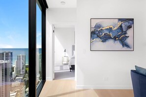 Ein modernes Hotelzimmer mit großem Fenster und Blick auf die Stadt, minimalistischer Einrichtung und einem gerahmten abstrakten Gemälde an der Wand.