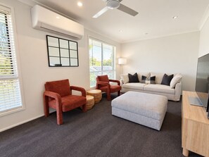 A modern living room with a sofa, two armchairs, a coffee table, a TV, and a ceiling fan. - Sawtell Garden House Dog Friendly Huge Yard Sleeps 6 (Sawtell)