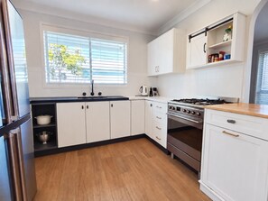 A modern kitchen with white cabinets, a stainless steel stove, and a wooden countertop. - Sawtell Garden House Dog Friendly Huge Yard Sleeps 6 (Sawtell)