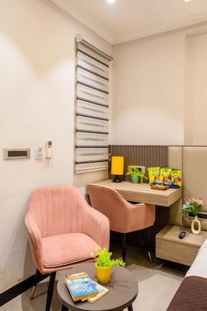 A compact hotel room with a bed, a desk with a chair, a small table with a lamp, a potted plant, and a wall-mounted radiator. - Hotel Vintage Villas  (New Delhi)