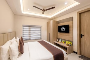 Ein Hotelzimmer mit Bett, Wandfernseher, Deckenventilator und Fenster mit Jalousien.