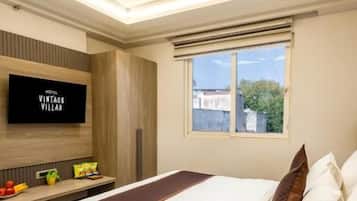 Habitación de hotel con cama, televisión, ventilador de techo, ventana y una pequeña mesa con una planta.