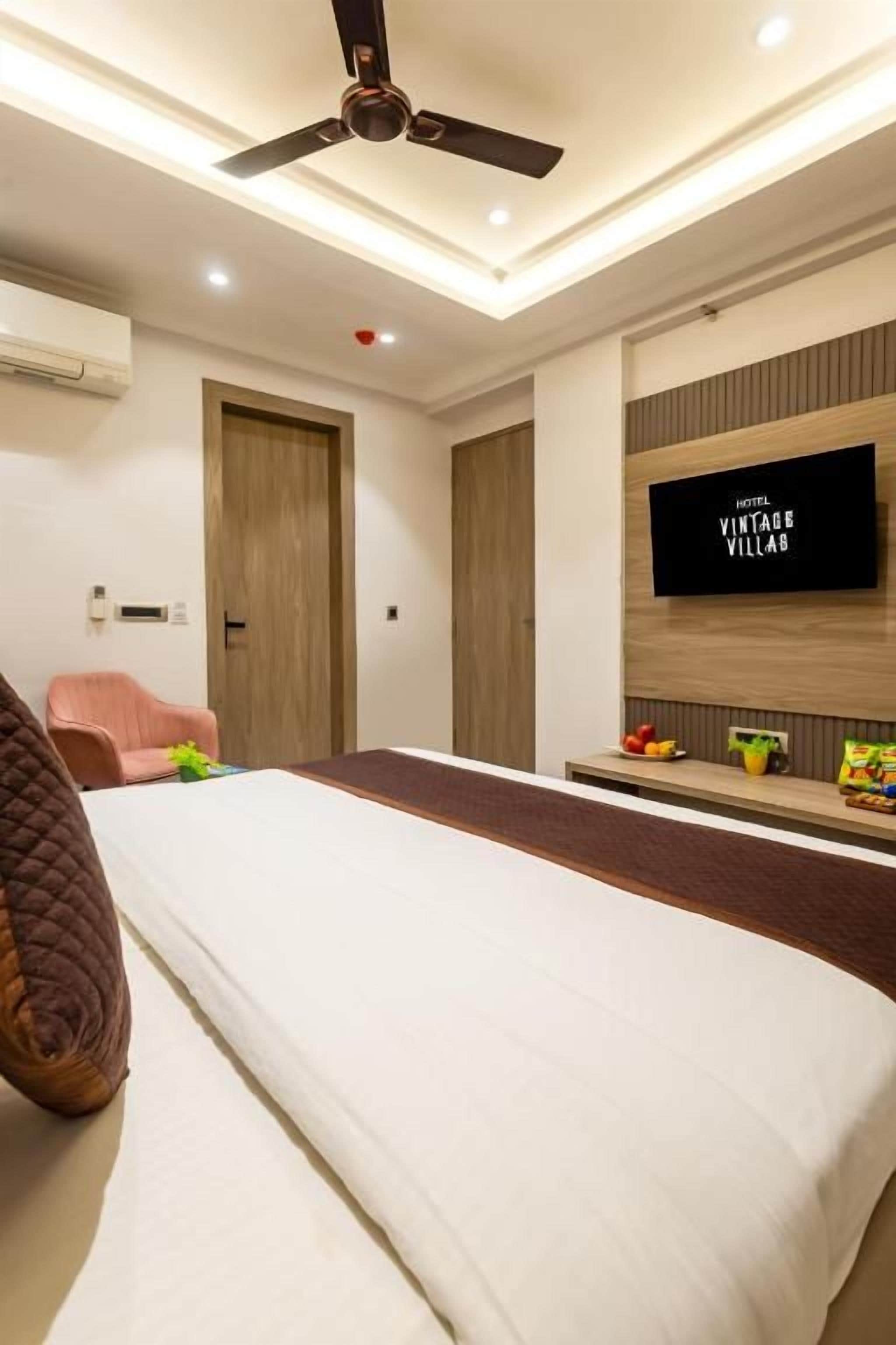 A hotel room with a bed, a ceiling fan, a television, and a small table with fruit.