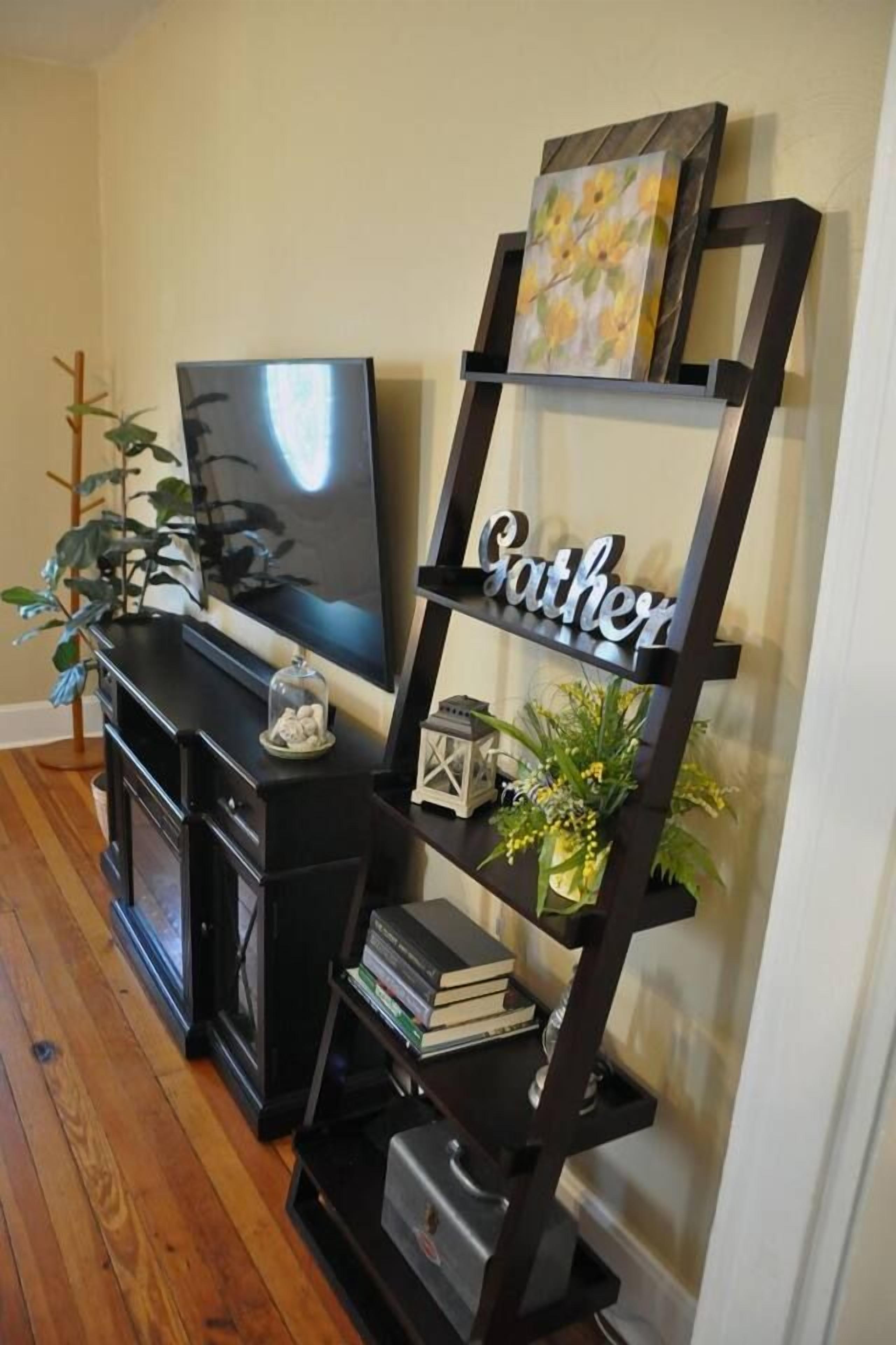 A living room with a flat-screen TV, a black entertainment unit, and a decorative black shelving unit with the word 'Gather' on it.