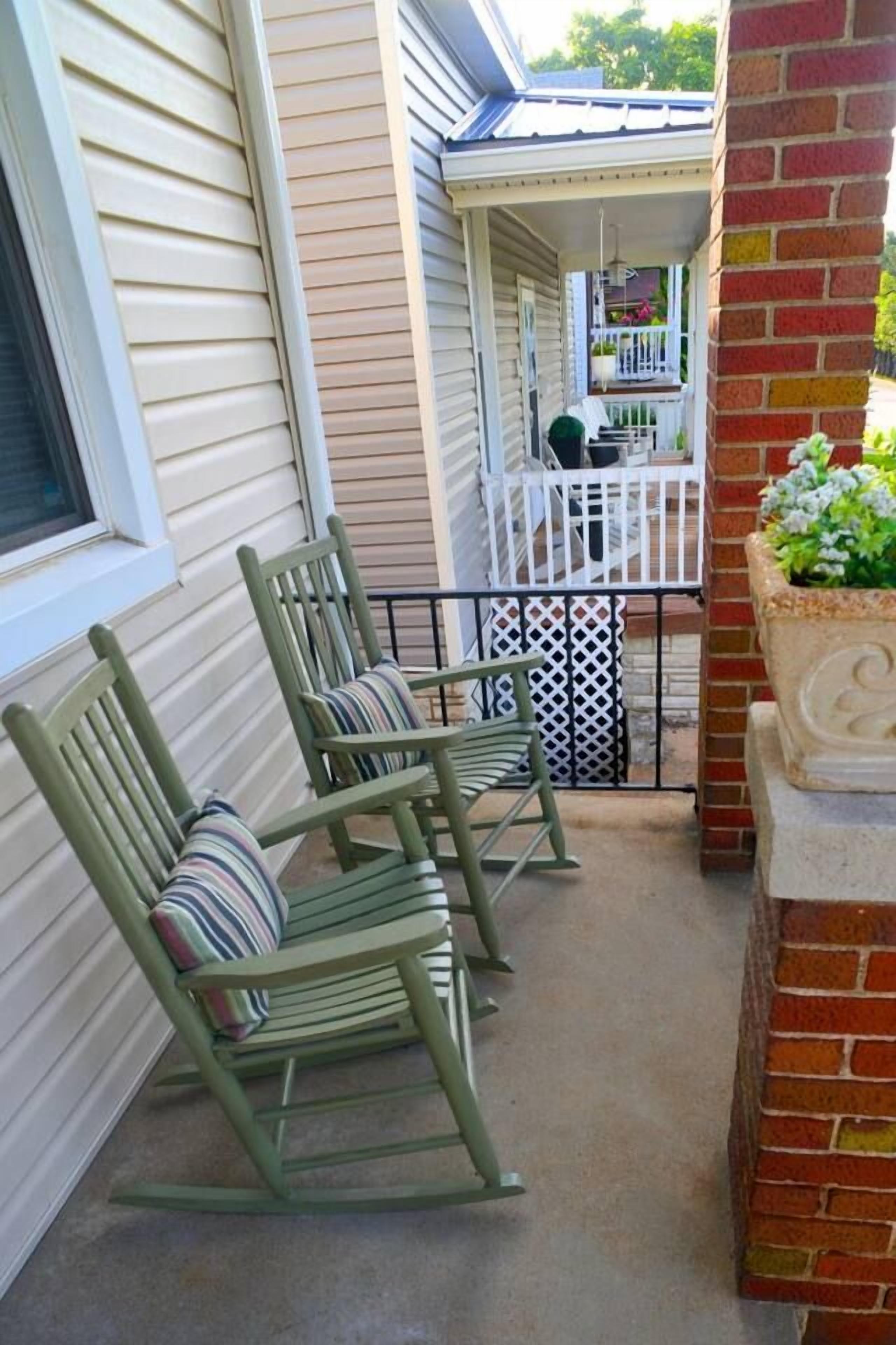 A porch with two rocking chairs, a white railing, and a planter with green foliage.