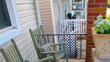 A porch with two rocking chairs, a white railing, and a planter with green foliage.