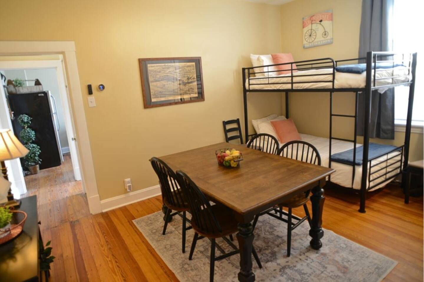 Une pièce avec un lit superposé, une table à manger avec des chaises et un tableau encadré au mur.