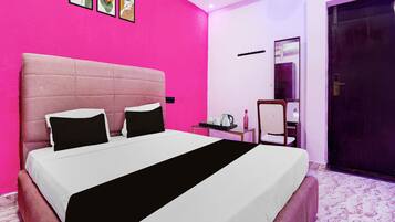 A hotel room with a large bed, a bedside table with a kettle, a chair, and a door.