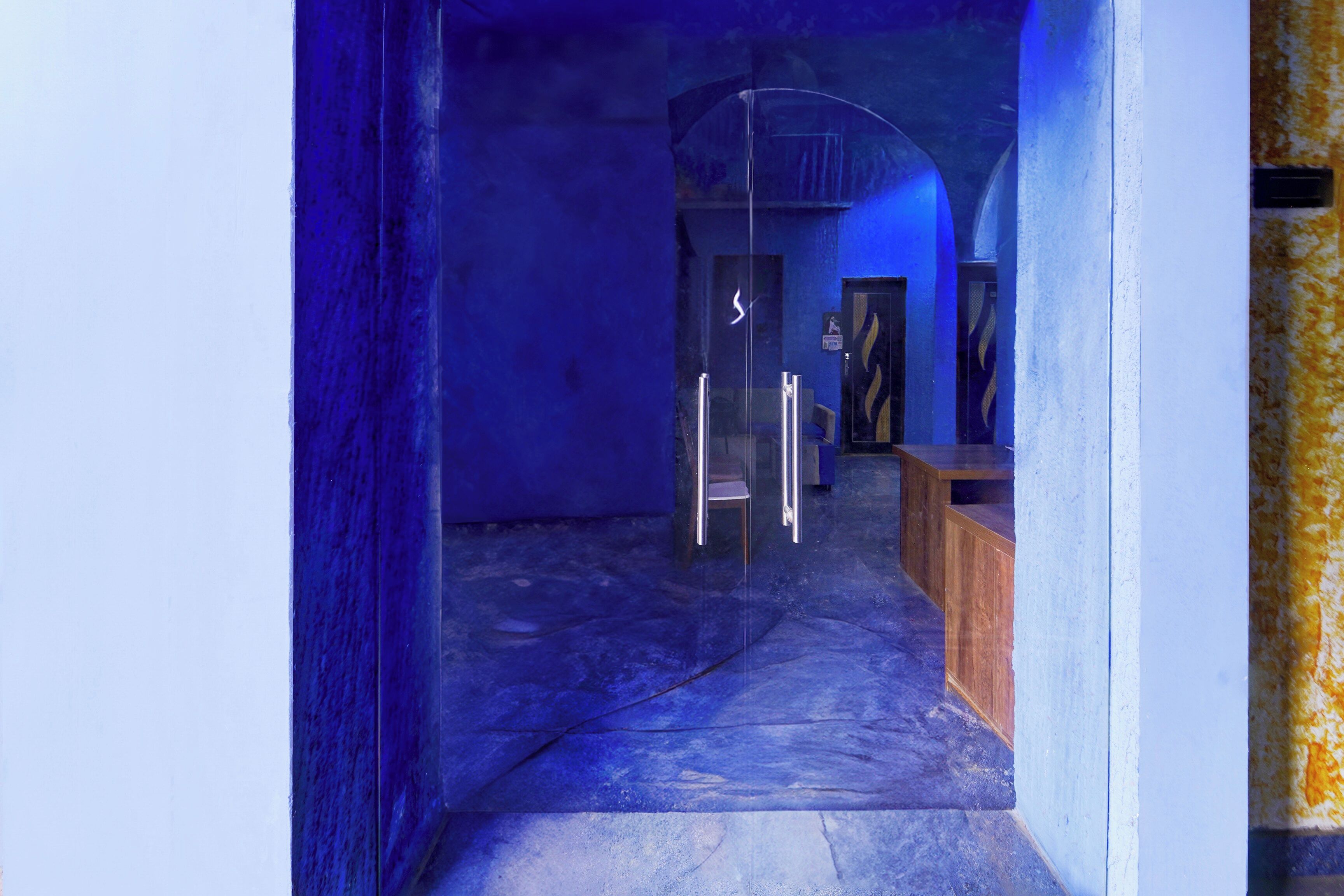 A corridor with a glass door leading to a room with a wooden bench and a chair.