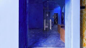 A corridor with a glass door leading to a room with a wooden bench and a chair.