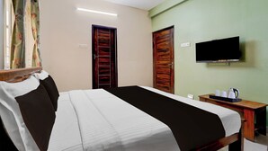A hotel room with a bed, a television, a desk with a kettle, and two doors. - Hotel Central Vishwanathapuram Formerly (Coimbatore)
