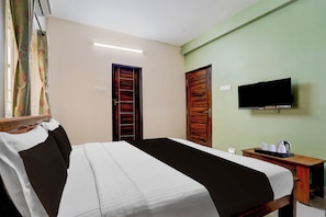 Ein Hotelzimmer mit einem Bett, einem Fernseher, einem Schreibtisch mit Wasserkocher und zwei Türen.