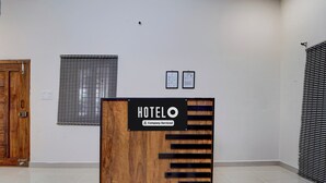 A hotel reception desk with a wooden finish and a sign indicating it is company-serviced. There are two framed certificates on the wall behind the desk. - Hotel Central Vishwanathapuram Formerly (Coimbatore)