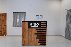 Ein Hotel-Rezeptionstresen mit Holzvertäfelung und einem Schild, das angibt, dass der Service geschäftlich ausgerichtet ist. Hinter dem Tresen hängen zwei gerahmte Zertifikate an der Wand.