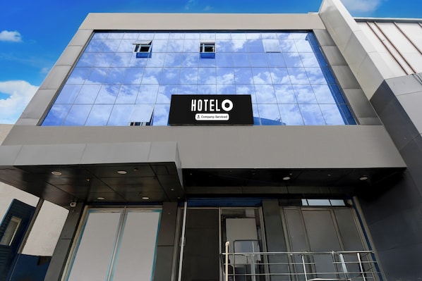 A hotel building with a clear sky reflected in the windows, a sign indicating it is a company-serviced hotel, and a modern architectural design. - OYO Ambedkar Gorakhpur Residency (Lucknow)