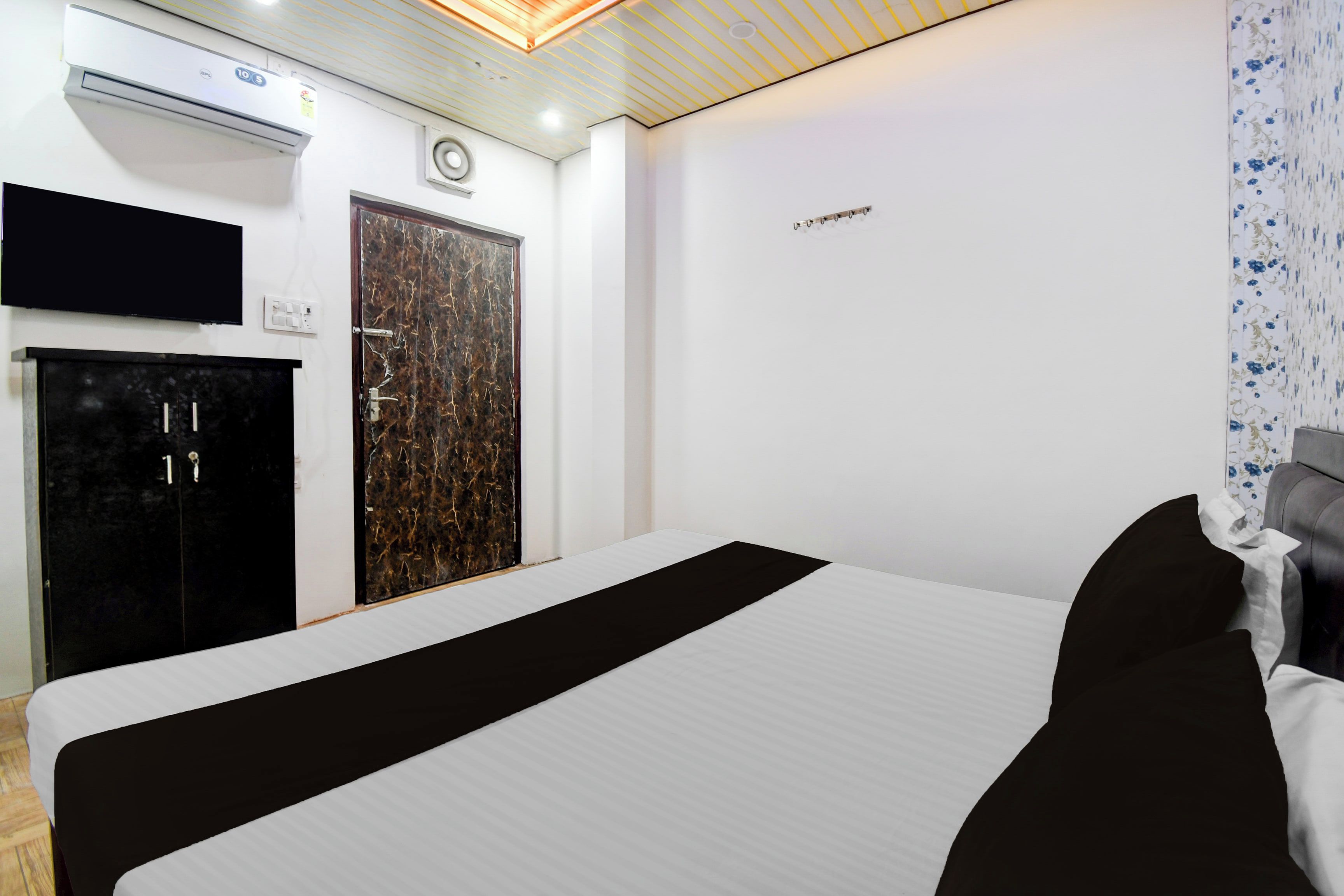 A hotel room with a bed, a wardrobe, a television, and a wall-mounted air conditioning unit.