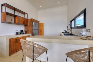 Eine moderne Küche mit Holdekor-Schränken, einem Edelstahl-Kühlschrank, einem eingebauten Backofen und einem großen Fenster. Zwei Korbstühle stehen an der Arbeitsplatte.